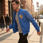 Dynamic city sidewalk scene capturing a male model in Porsche varsity jacket mid-motion, demonstrating its windbreaker features and functional pockets.