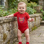 Full-body shot of baby in romper standing against a stone wall in a garden, emphasizing fit and playful stance.