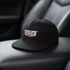 Close-up of small Cadillac Car Snapback Hat on black leather surface, focusing on cotton weave and snapback closure.