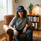 Model wearing Cadillac Car Snapback Hat in a cozy indoor environment, showcasing fit and stylish design with warm-toned decor.