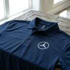 Close-up of men's Mercedes-Benz polo draped over rustic wooden table, emphasizing fabric texture and detailed stitching.