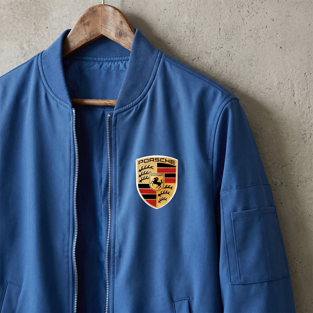 Close-up of men's Porsche bomber jacket hanging on a rustic wooden hanger against a concrete background, emphasizing the softshell material and structured ribbed cuffs.
