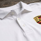 Close-up of Porsche Dry Blend Polo front placket with dyed buttons on wooden background, highlighting fabric weave and finish.