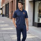 Male model in navy Porsche polyester polo standing on city sidewalk, showcasing athletic fit and breathable fabric in urban setting.