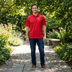 Man wearing men's Porsche polyester polo in a relaxed outdoor setting, showcasing athletic fit and polished style with greenery background.