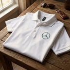 Neutral-colored Mercedes-Benz polo laid on rustic wooden table with soft indoor window light emphasizing fabric details.