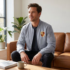 Male model seated in a minimalist living room wearing Porsche windbreaker with partially open zipper, emphasizing lightweight breathable fabric and relaxed fit.