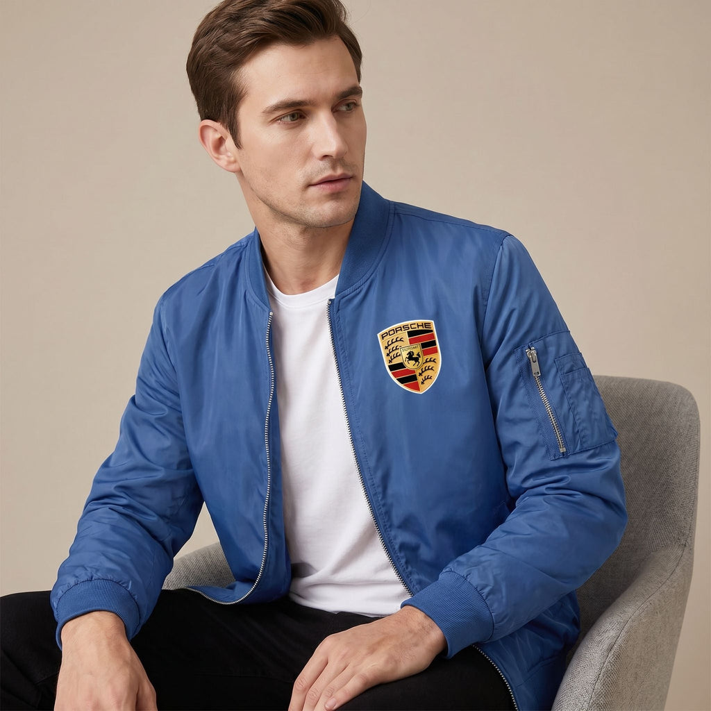 Indoor studio image of male model seated in a white Porsche bomber jacket, highlighting its textured fabric, structured fit, and versatile style.