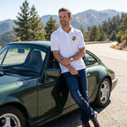 Male model in white Porsche polyester polo in outdoor setting, emphasizing breathability and modern design under sunny light.