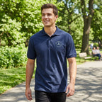 Man in white Mercedes-Benz polo walking in park, showcasing relaxed fit and breathable moisture-wicking fabric.