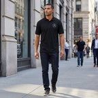 Full-body view of a male model wearing the Mercedes-Benz polo on a city sidewalk, showcasing fit and casual style in natural daylight.