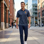 Man in navy large Porsche polyester polo strolling on city sidewalk, highlighting modern fit, style, and versatility with city architecture background.