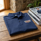 Neatly folded Men's Cadillac Car Dry Blend Polo on wooden surface with magazines, highlighting fabric texture, welt collar, and craftsmanship.