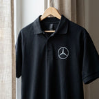 Close-up of men's Mercedes-Benz DryBlend polo hung on a natural wooden hanger, highlighting fabric texture and collar details.