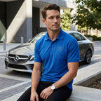 Black Mercedes-Benz polo placed on concrete ledge beside a parked car, featuring relaxed fit and moisture-wicking fabric on model seated outdoors.