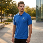 Male model wearing white Mercedes-Benz polo in city outdoor setting during golden hour, showcasing classic fit and structured collar.