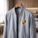 Close-up of men's Porsche bomber jacket hanging on a wooden hanger, highlighting softshell fabric, ribbed cuffs, and full-zip front in natural light.