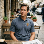 Candid shot of man in Porsche polyester polo at outdoor cafe, highlighting breathable fabric and relaxed fit in cozy street scene.