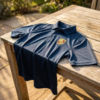 Porsche men's polyester polo draped over outdoor wooden table, emphasizing fabric texture and fade-resistant stitching.