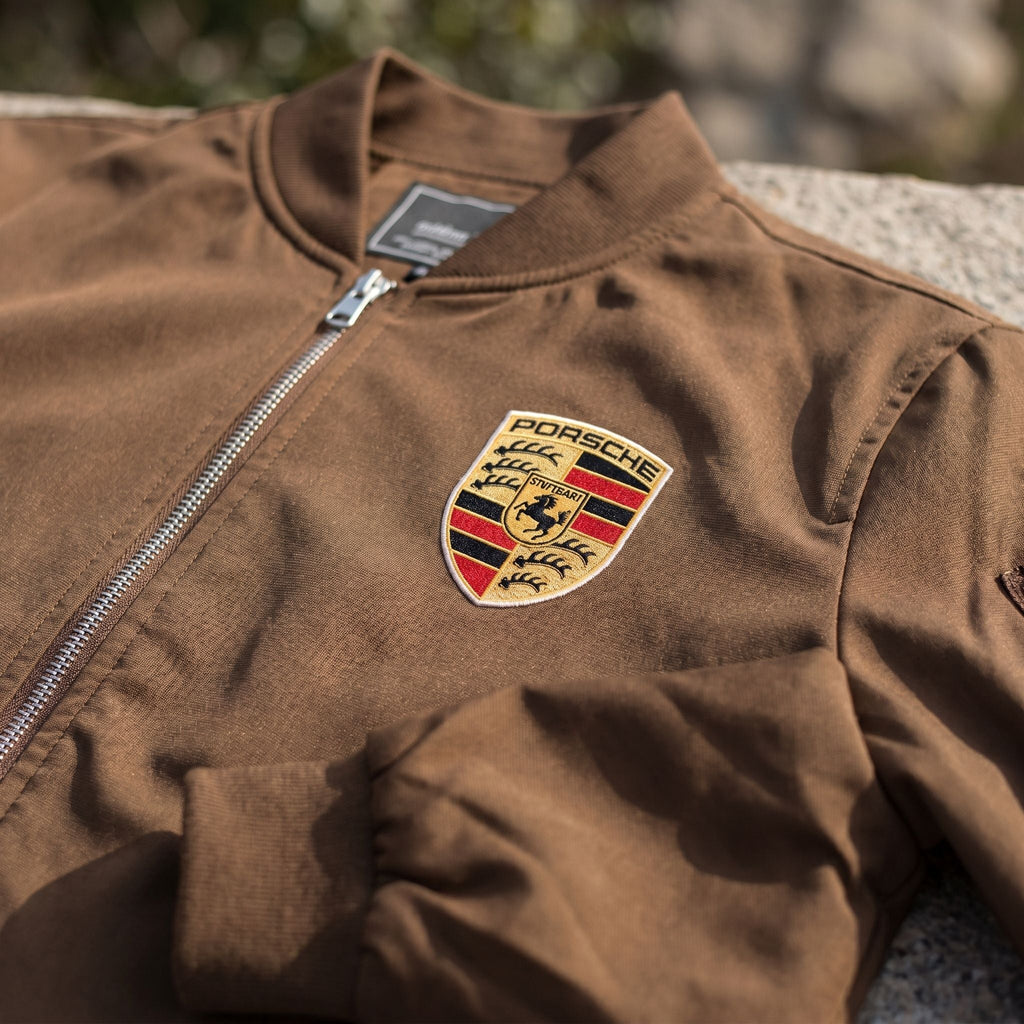 Close-up of men's Porsche bomber jacket showing textured softshell fabric with subtle sheen and ribbed collar.