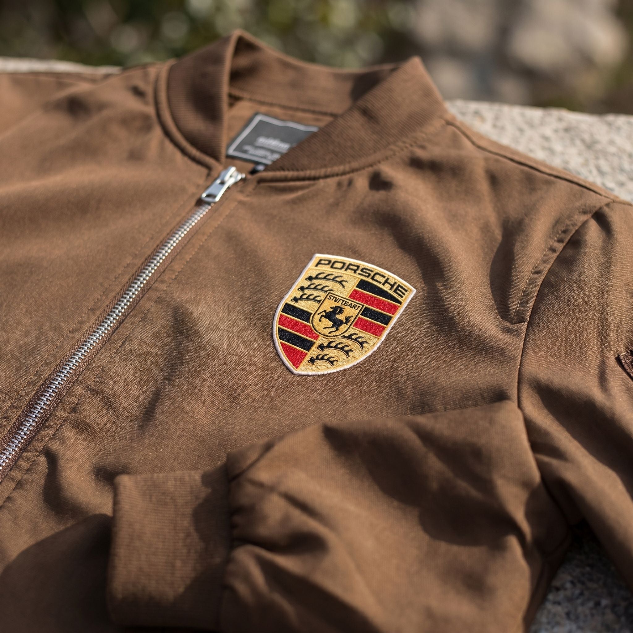 Close-up of men's Porsche bomber jacket showing textured softshell fabric with subtle sheen and ribbed collar.