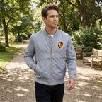 Model walking in a park wearing white Porsche varsity windbreaker, highlighting lightweight design, stylish fit, and outdoor versatility in soft daylight.