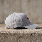 Side view of a small Cadillac Car Dad baseball cap on a rustic concrete surface, highlighting sewn eyelets and buckle closure with natural lighting.