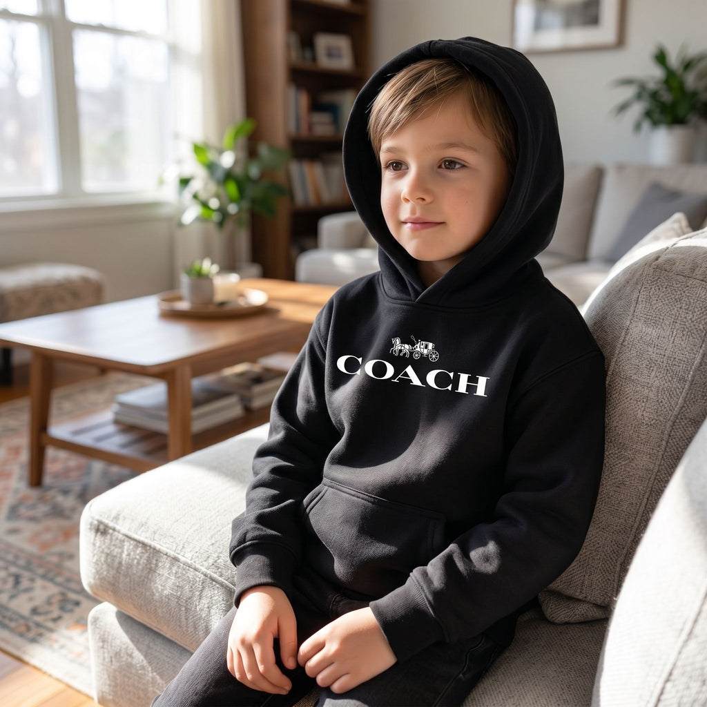Child seated in a living room wearing youth kids coach pullover hoodie, focus on fabric texture and comfortable fit in natural indoor light.